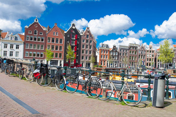 Naklejka premium Amsterdam, the Netherlands-April 27: Amsterdam cityscape with apartment houses and bikes parked on the bridge on April 27,2015. Amsterdam is the most populous city of the Kingdom of the Netherlands.