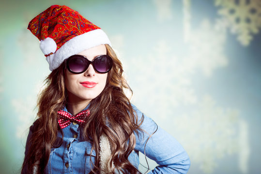 Funny smiling hipster girl in sunglasses wearing santa hat 