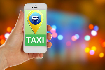 Hand holding mobile smart phone with interface taxi on night background