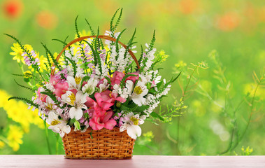 Beautiful wildflowers in wicker basket on field background