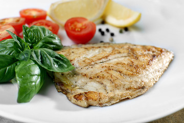 Dish of fish fillet with basil and lemon on plate close up