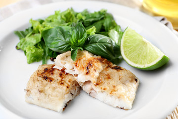 Dish of fish fillet with greens and lime on table close up