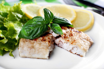 Dish of fish fillet with greens and lemon on plate close up
