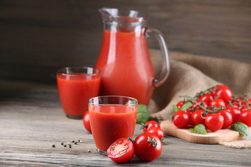 Full jug and glasses of tomato juice with vegetables on wooden table close up
