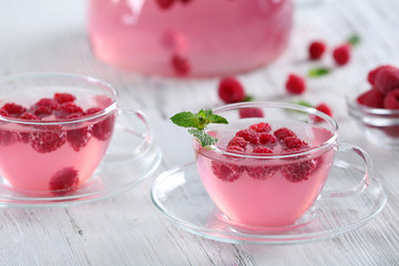 Cups and teapot of raspberry drink with berries on wooden table close up
