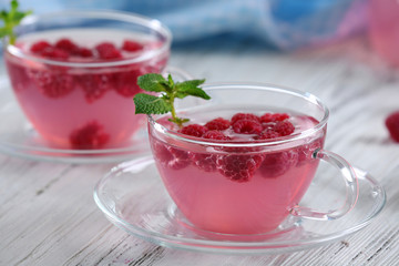 Cups and teapot of raspberry drink with berries on wooden table close up