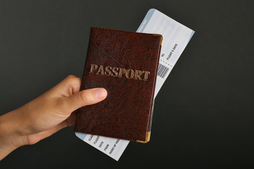 Female hand holding passport and ticket on dark background