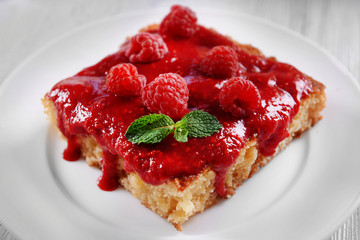 Fresh pie with raspberry jam in white saucer on wooden table, closeup