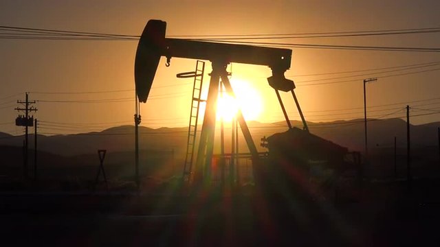 An oil derrick pumps against a sunset sky.