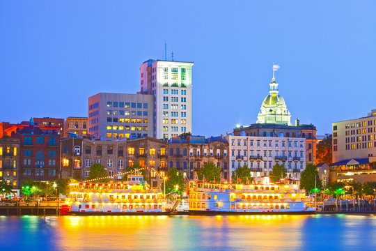 Savannah Georgia USA, skyline of historic downtown at sunset with illuminated buildings and steam boats