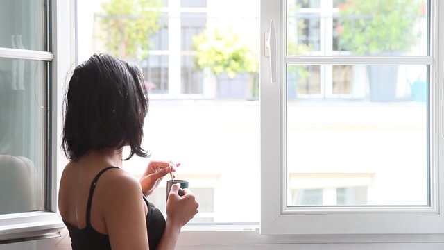 woman standing at an open window with cup