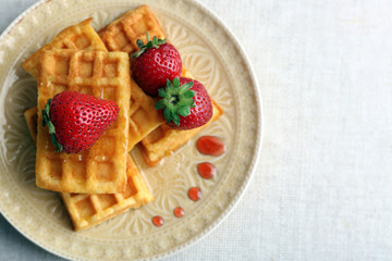 Sweet homemade waffles with fresh strawberries on plate, on light background