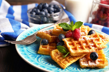 Sweet homemade waffles with forest berries and sauce on table background