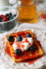 Sweet homemade waffles with forest berries on plate, on light background