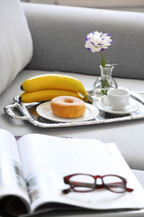 Light breakfast and magazines on sofa in living room, close up