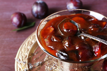 Tasty homemade plum jam in glass saucer on metal tray on wooden table, closeup