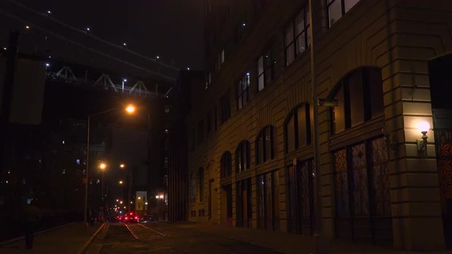 Establishing shot of warehouses under the Brooklyn Bridge with subway train crossing.