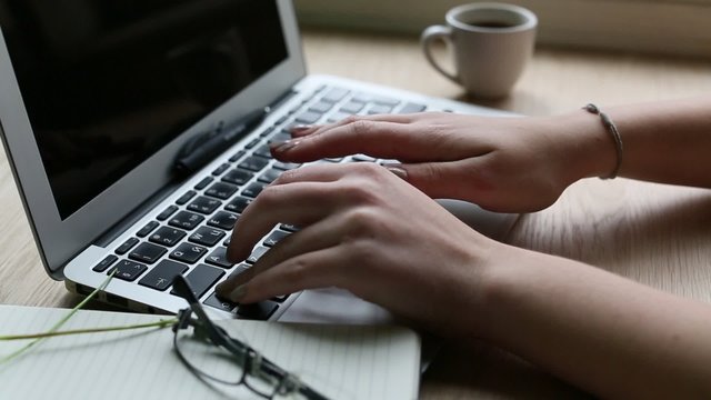 Women's fingers typing on laptop keyboard.
