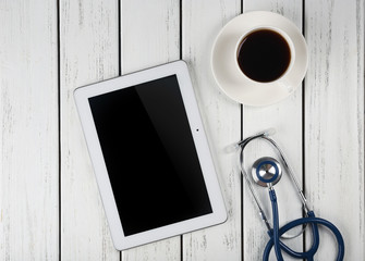 Blank tablet, stethoscope and cup of coffee on wooden background
