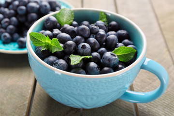 Cup and plate with fresh blueberries on wooden table close up