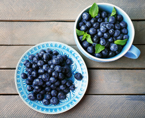Cup and plate with fresh blueberries on wooden table close up