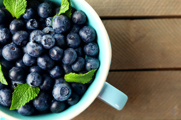 Fresh blueberries in cup on wooden table close up