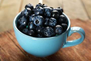 Fresh blueberries in cup on wooden table close up