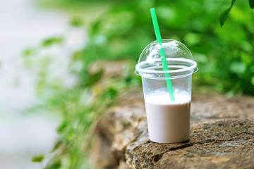 Plastic cup of milkshake on green background, outdoors