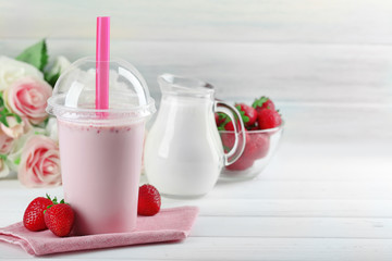Plastic cup of milkshake on light wooden background