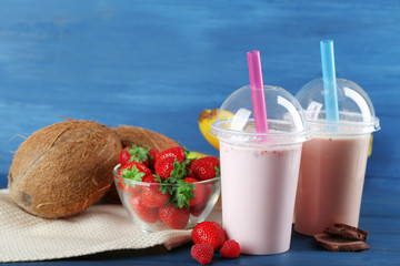 Plastic cup of milkshake with banana on color wooden background