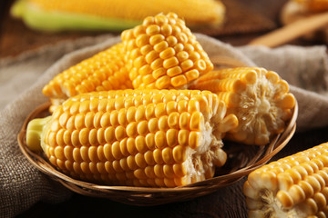 Ripe corn in wicker bowl on wooden background