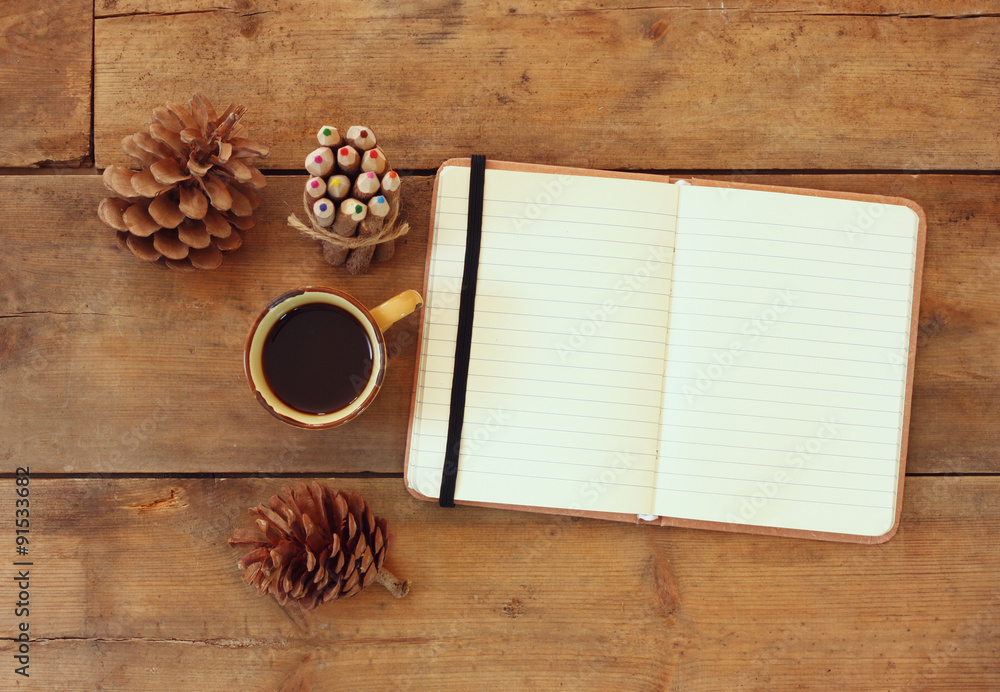 Poster top image of open notebook with blank pages, next to pine cones and cup of coffee over wooden table.