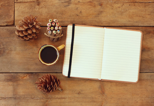 top image of open notebook with blank pages, next to pine cones and cup of coffee over wooden table. retro filtered image
