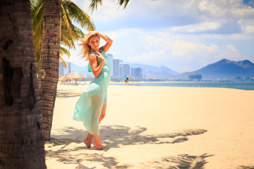 blonde girl in azure with hands above head near palms on beach