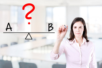 Young business woman writing A and B compare on balance bar. Office background.