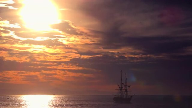 A tall clipper ship sails at sunset.