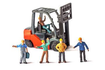 selective focus of miniature worker standing front of forklift machine, on white background.
