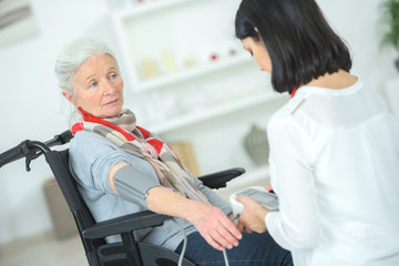 Obraz premium Old lady in a wheelchair having her blood pressure taken