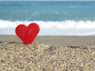 Red heart on white sand beach