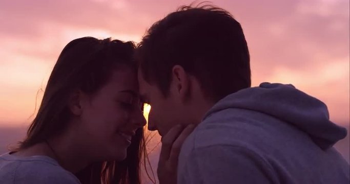 Happy loving couple kissing at sunset showing emotional intimacy touching hugging and cuddling