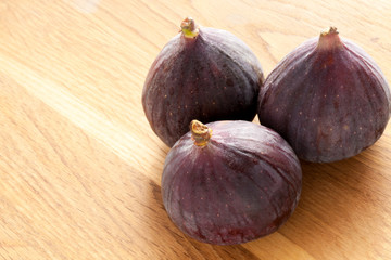 Three whole fresh figs on a light wooden surface.