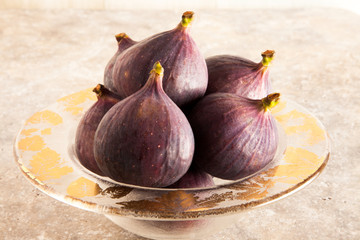 Whole fresh figs in a glass bowl on a ceramic tile surface.