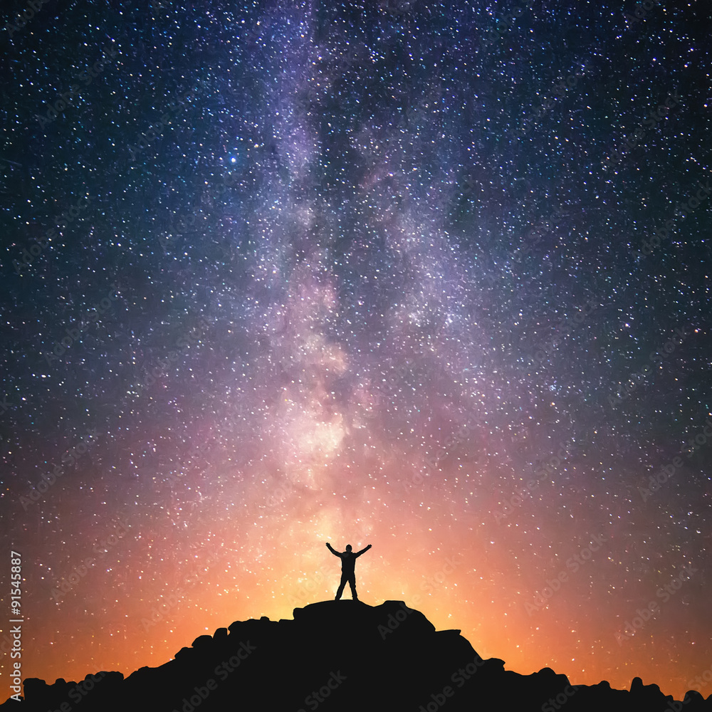 Wall mural man and the universe. a person is standing on the top of the hill next to the milky way galaxy with 