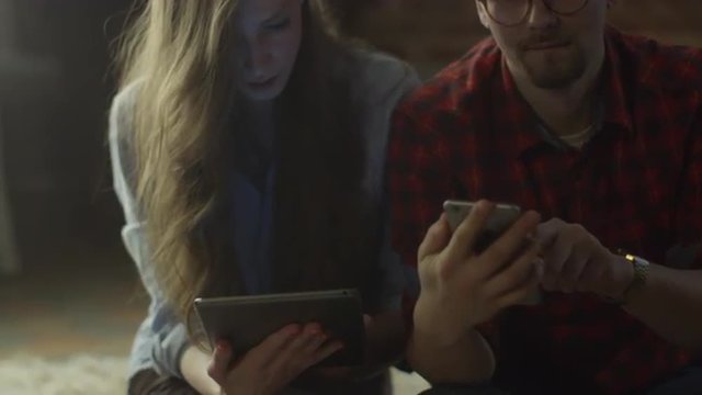 Young Couple Using Mobile Devises At Home At Evening