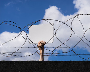Mann hält leeres Schild über Absperrung aus Beton und Stacheldraht