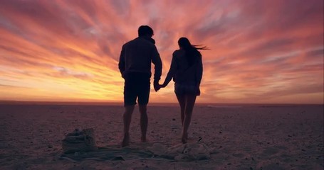Happy couple walking towards sunset on empty beach dramatic orange sky in background RED DRAGON - Powered by Adobe