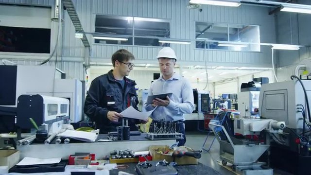 Engineer in Hard Hat and Factory Worker are Talking about Blueprint