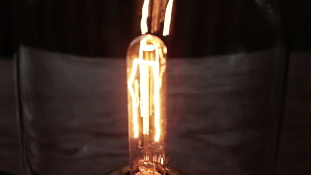 An old retro style light bulb fixture lights up brightly in the dark, out of focus
