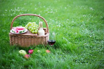picnic basket with fruits and glass of wine on green grass