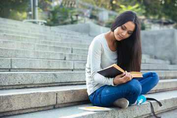 Girl sitting on the city stairs and reading book outdoors